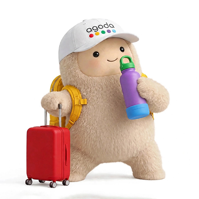 Jolly, from Meta's Muse, is shown wearing a cap with the Agoda logo and holding a water bottle next to a suitcase. Jolly, from Meta's Muse, is shown wearing a cap with the Agoda logo and holding a water bottle next to a suitcase.